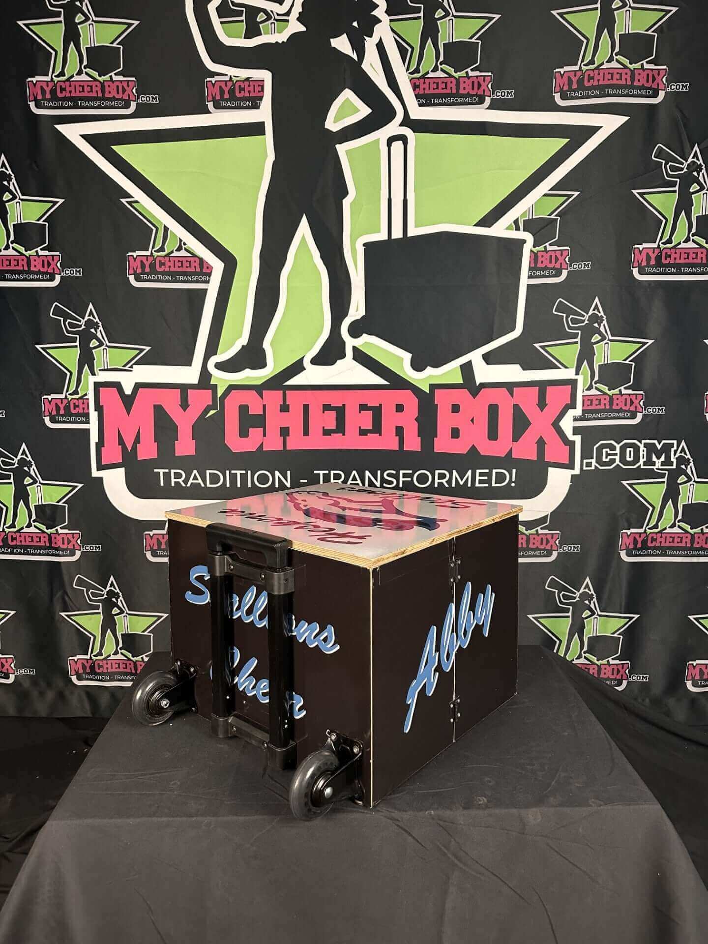 Fully customizable collapsible cheer box with wheels and personalized design in front of My Cheer Box backdrop.